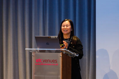 Decorative image: photo of Henny Bird. She is standing at a podium smiling.