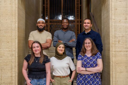 Image of six TSP trainees standing in two rows, on steps outside the Liverpool HMRC office. All smiling at the camera.