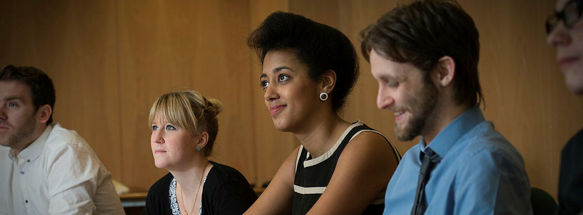 Photo of colleagues sitting together at a table, listening to a speaker