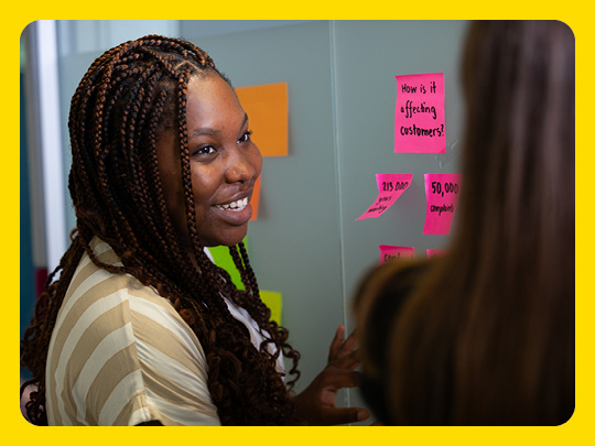 Image shows a person standing by a wall and working with post-it notes on the wall