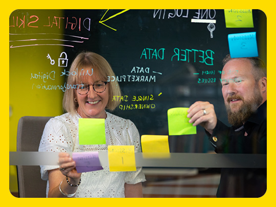 Image shows two people behind a glass wall working with post-it notes