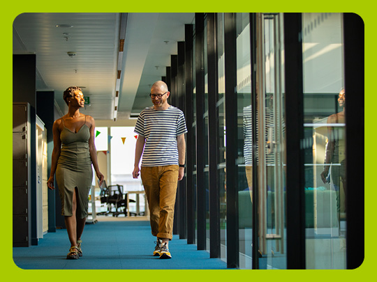 Image shows two people walking in glass walled corridor