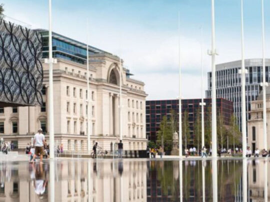 An impressive limestone-coloured building with modern architectural influences set within a grand square.