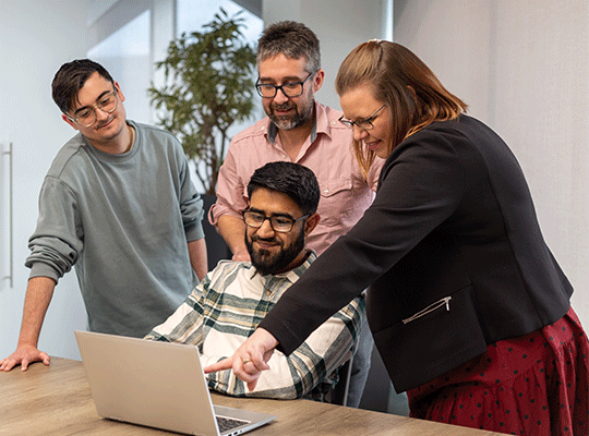 Group of colleagues gathered round a laptop, pointing at the screen