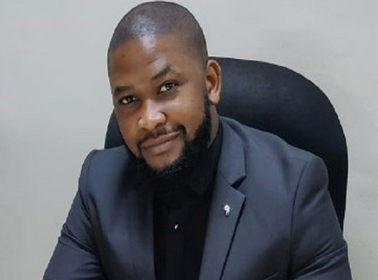 Boaz sitting in a chair, wearing a suit, looking the camera.