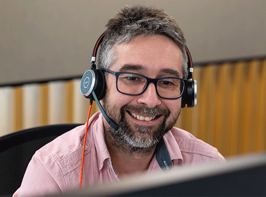 Man looking at the computer screen smiling and wearing a headset talking to a customer