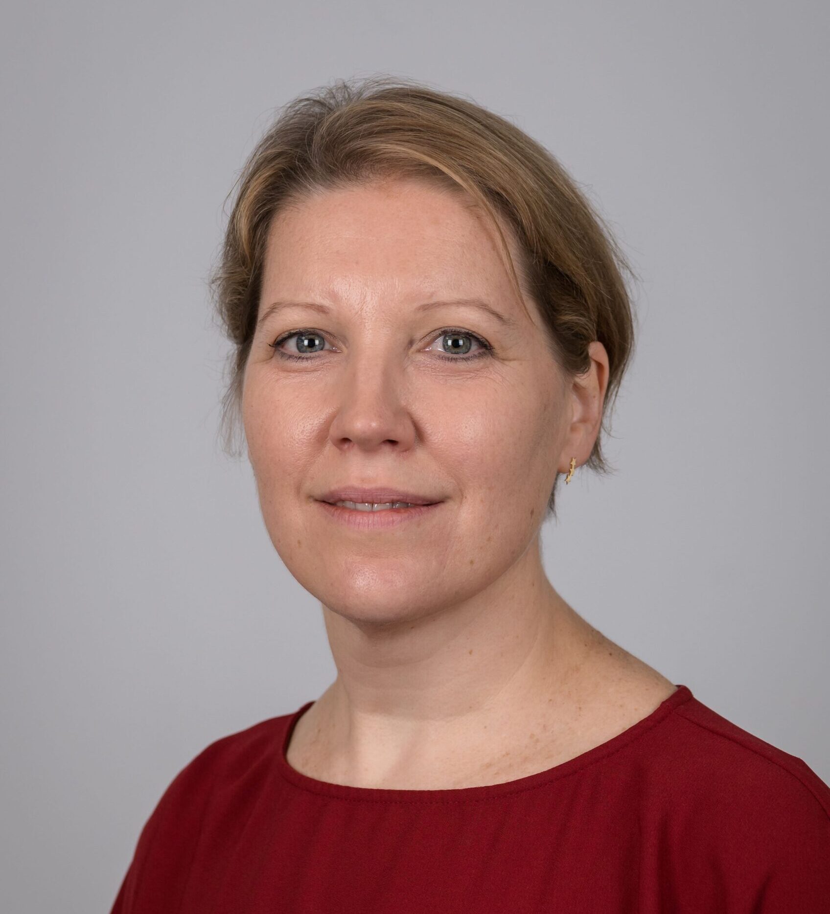 Portrait of Caroline Hacker, the Chief Operating Officer for the Northern Ireland Office. She wears a red top and has her hair tied back.