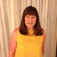 A photo of Christine Tomlinson, she has dark brown hair, is wearing a yellow sleeveless top, and is smiling