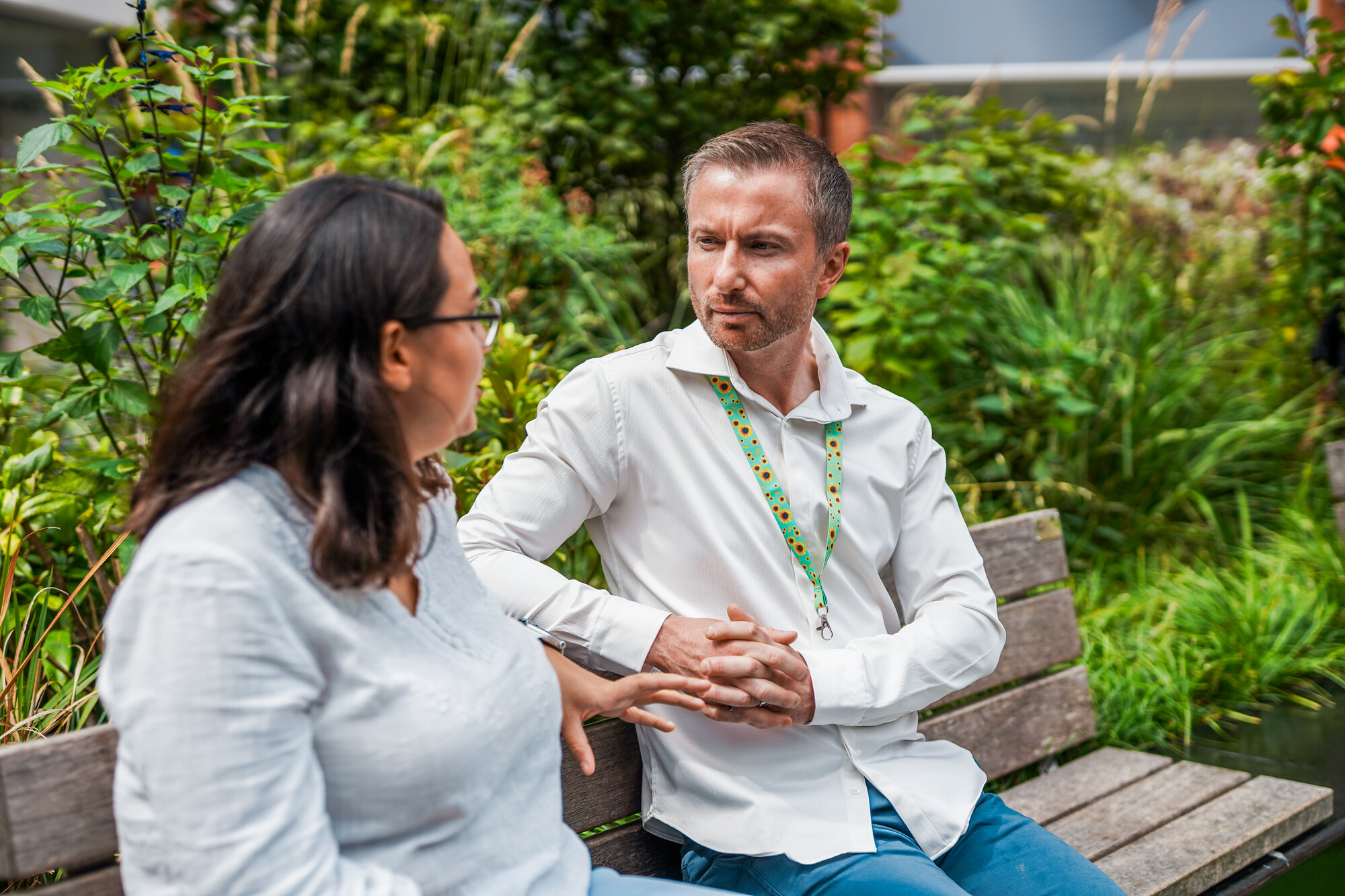 A man with a less-visible disability sitting outside with a colleague, he is wearing a sunflower lanyard.