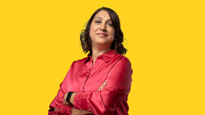 DWP colleague smiling at the camera. She has her arms folded. She is stood against a yellow background.