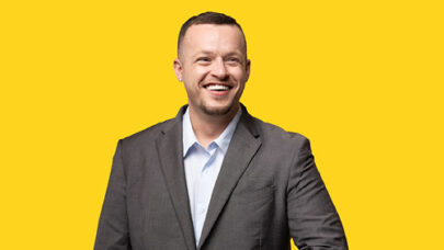 DWP smiling. He is stood against a yellow background.