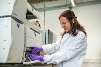 A photo of a female scientist, she is wearing purple latex gloves and is focused on a task