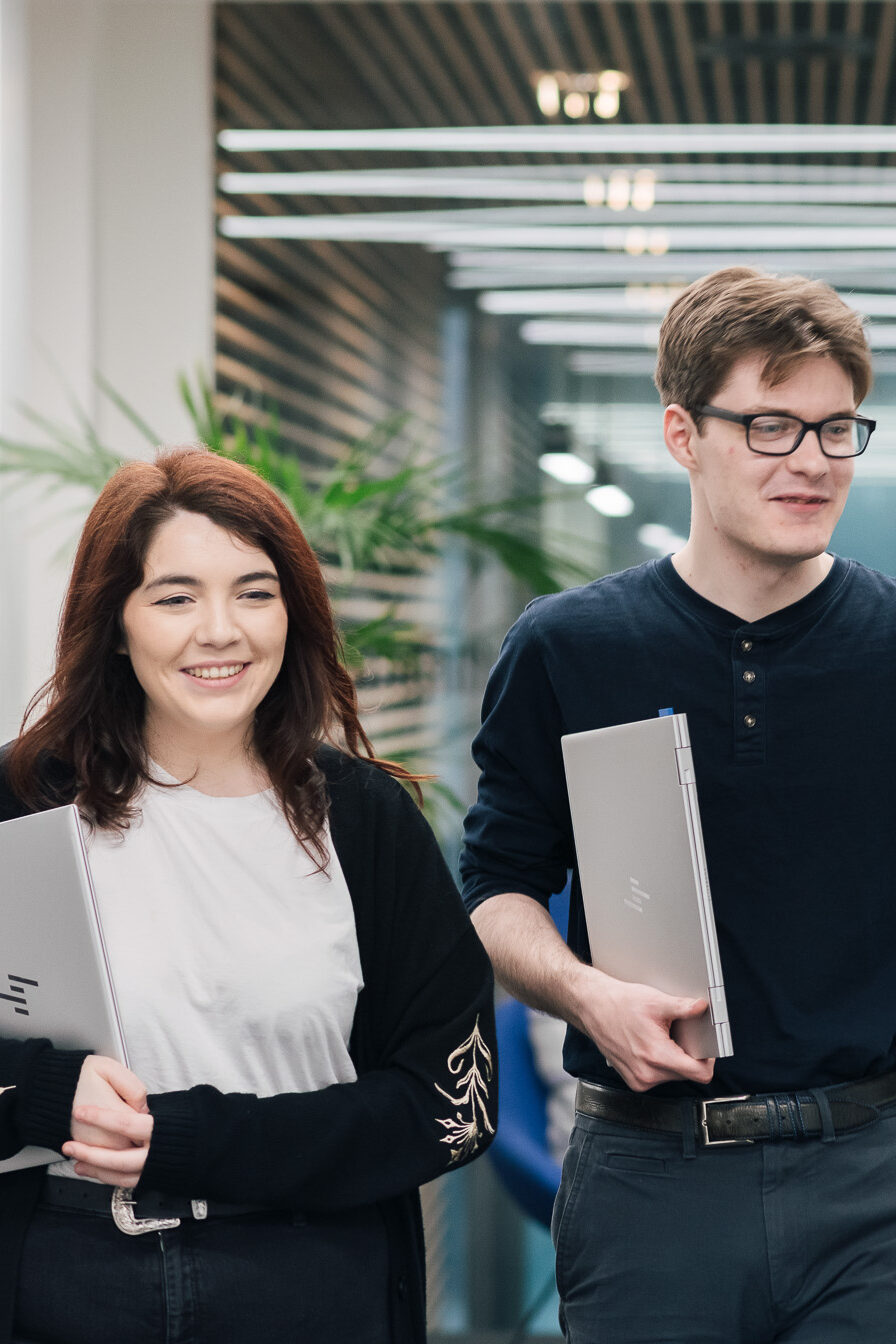 HMRC colleagues walking down a corridor, chatting, carrying laptops.