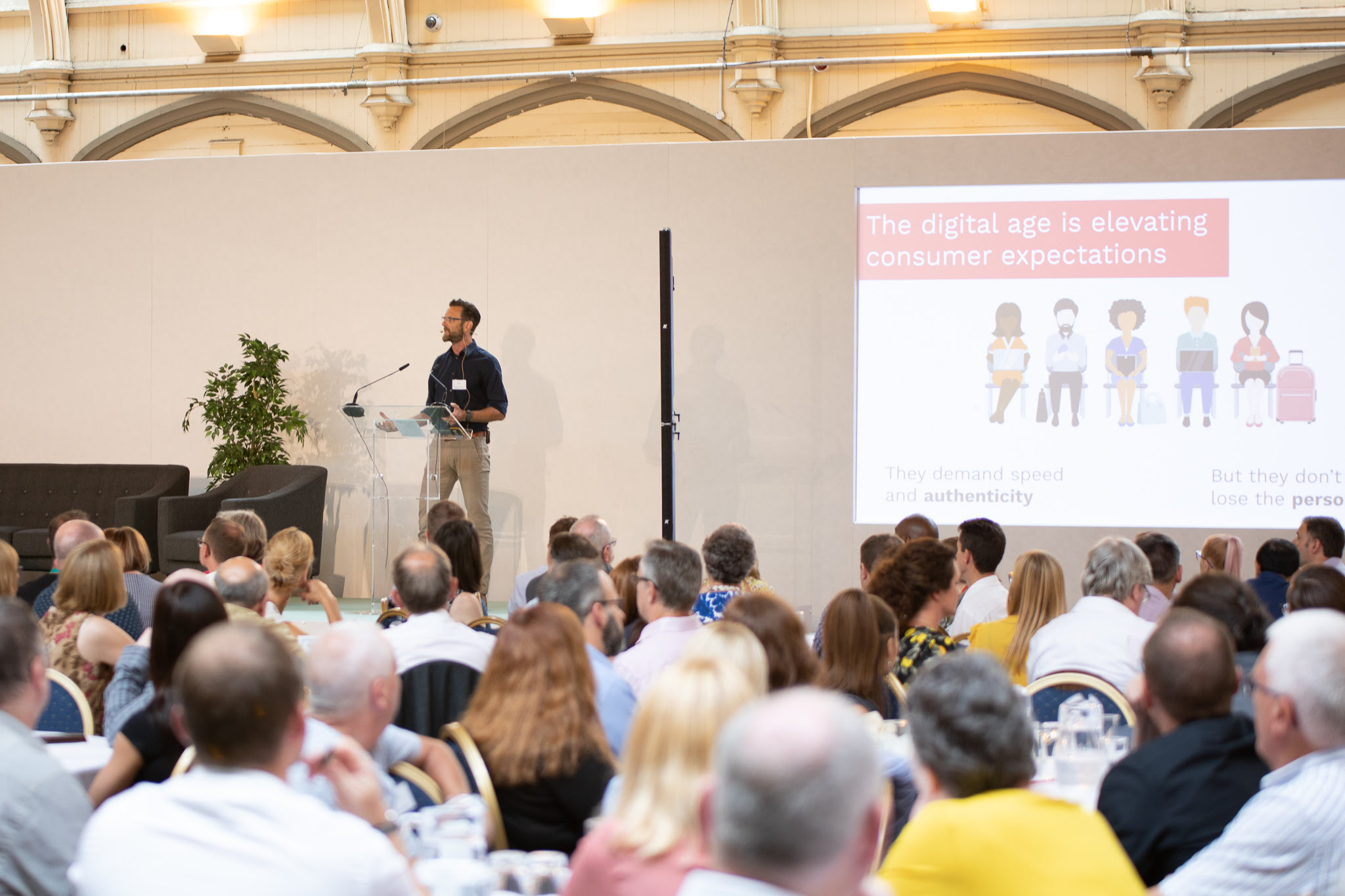 A man on a stage, before an audience, presenting on consumer expectations in the digital age.