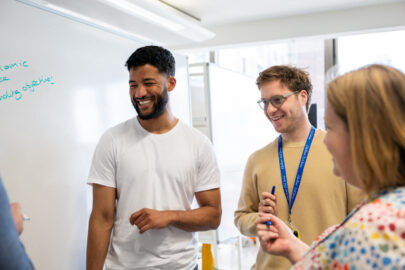 Decorative image: three colleagues standing by a whiteboard together. They are smiling and talking.