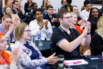 Decorative image: a photo of a conference audience, they are sitting at tables and applauding.