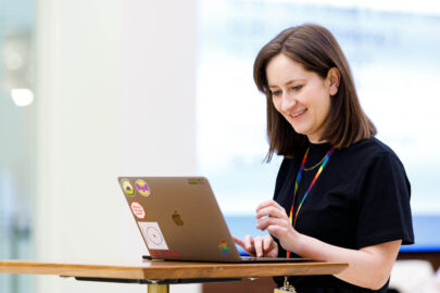 Decorative image: A woman working on her laptop at a stand up desk, she is wearing a rainbow lanyard.