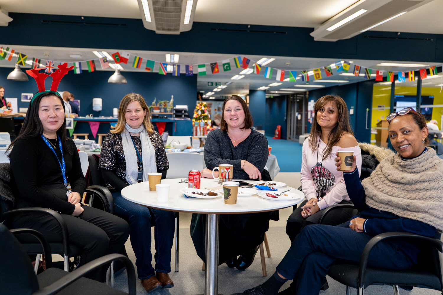 Decorative image: Five (5) women sitting around a table together drinking coffee