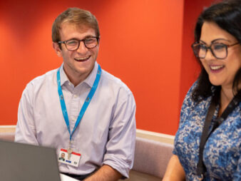 Two colleagues working together on a single laptop screen.