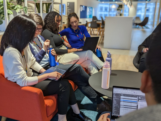 A group of colleagues sitting together on a red sofa, looking at laptops