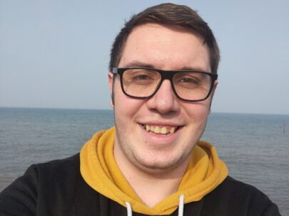 photo of Matthew. He is wearing a yellow hoodie and the ocean is in the background.