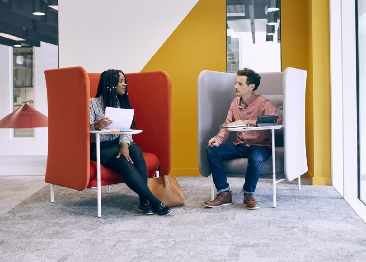 Two people sitting in an office space with laptops, chatting