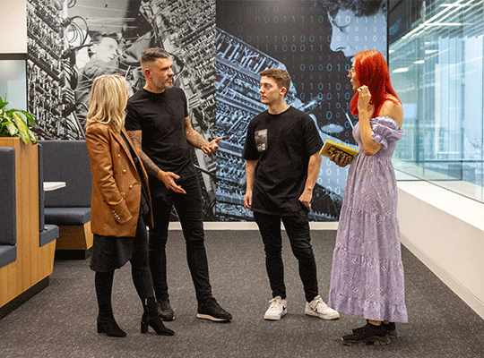 Four young colleagues standing together in a modern office space. They are dressed casually.