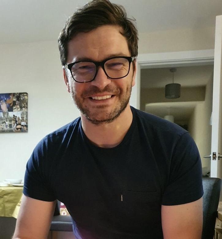 Image of Mike Harrison wearing dark rimmed glasses and a black t-shirt smiling directly at the camera.