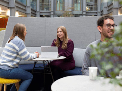 Colleagues sat around a table in a relaxed environment, with one typing on a laptop