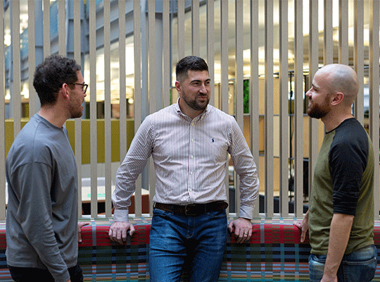 Three male colleagues in the Newcastle office. They are standing and chatting together.