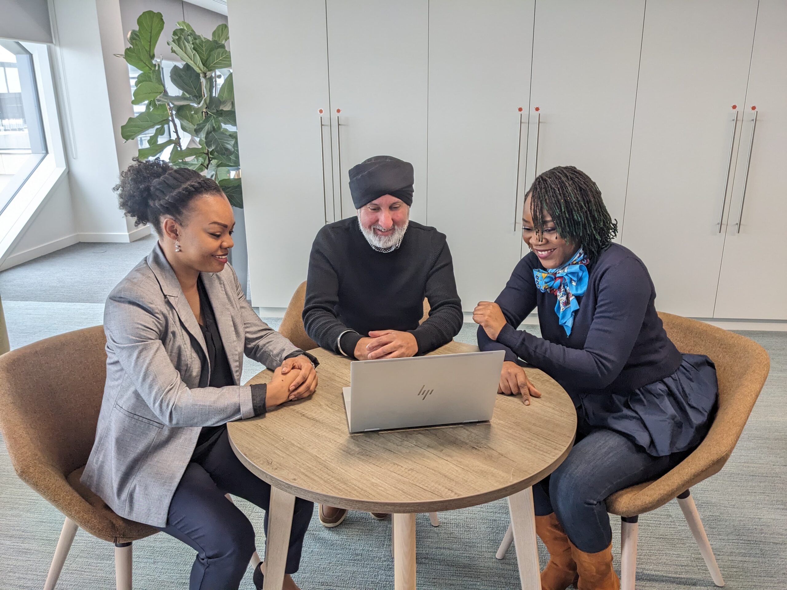 Image of HMRC colleagues sitting at a round desk, looking at a laptop.