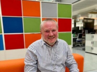 HMRC employee, Peter sitting on a sofa, smiling at the camera with a colourful wall behind him