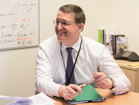 Decorative image: A photo of Rupert McNeil GCPO, he is dressed in a shirt and tie and is smiling to someone off-screen