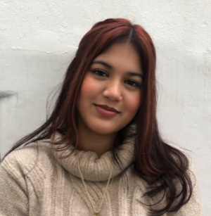 Photo of Samaira Uddin. She has long auburn hair in a middle-part, and is wearing a cream cowl-necked sweater