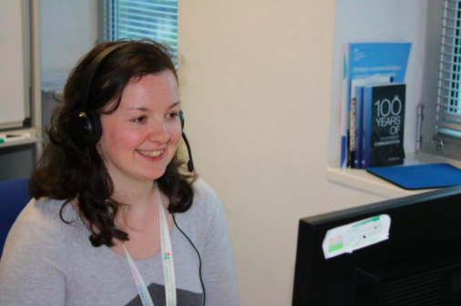 A photo of a call centre worker, speaking on a headset and looking at a computer.