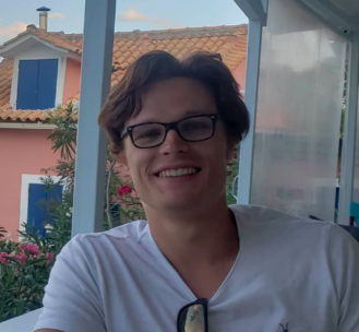photo of Murray Lane. He has longish blonde hair in a middle-part and is wearing rectangular glasses, and a white tshirt.