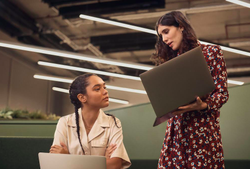 Decorative image: two people looking at laptops, they are both women, smartly dressed and are in conversation.