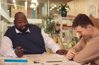 Decorative image: a t-level student meeting with his tutor. They are both men and are sitting at a table strewn with paperwork, both are laughing and look relaxed.