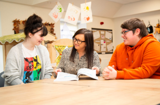 Decorative image: two t-level students with their tutor, they are smiling and talking together.