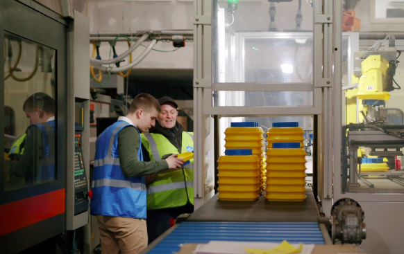 Decorative image: two people wearing hi-vis vests, working in a workshop environment. They are looking at a piece of equipment and are in conversation.