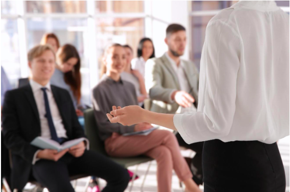 Professionally dressed people, sitting down, listening to someone speak