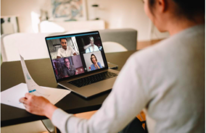 A woman looking at her laptop screen, which shows a zoom call with four colleagues present