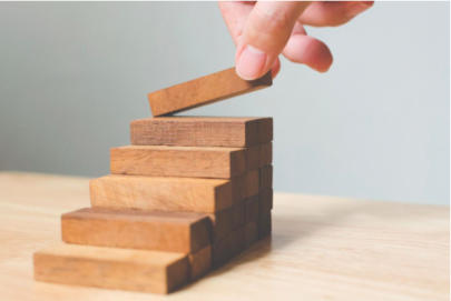 A perspn's hand building a stairway from wooden blocks