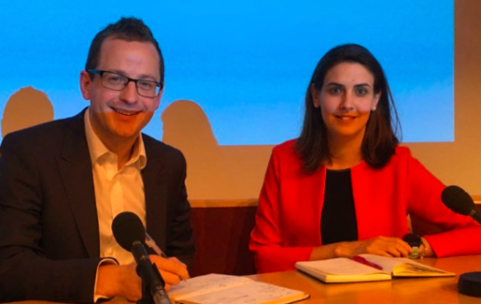 Decorative image: Photo of Richard Ney and Helen Mills, Department for Exiting the EU. They are on a stage at an event, both have microphones before them and open notebooks.