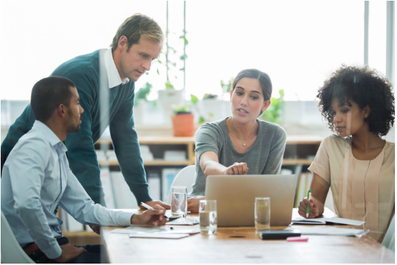 Colleagues in a meeting. They are leaning to look at a laptop screen and in a dynamic discussion