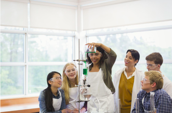 A group of young people conducting a science experiment by pouring from one flask, into another