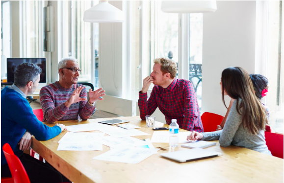 A group of teachers in a meeting, with lots of documents spread on the table they are sitting at