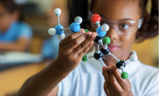 A girl wearing protective goggles, holding a model of molecules