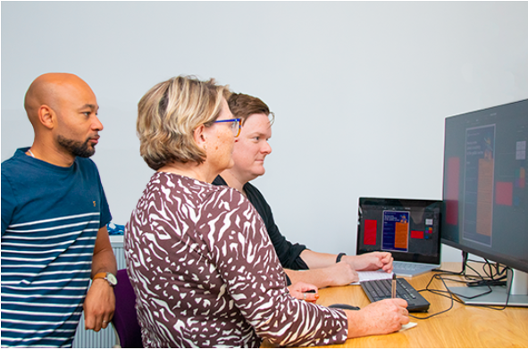 Three people sitting together, looking at a computer on a desk