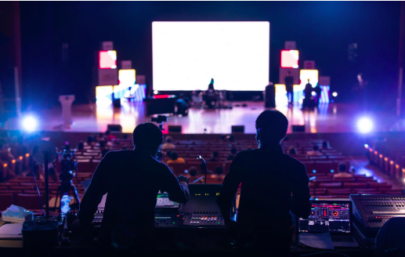 Two people silhouetted at a sound desk, looking towards a brightly lit stage